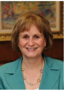 Woman with light brown shoulder length hair in green blazer smiles at camera.