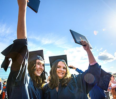 Graduates in gaps and gowns holding up diplomas