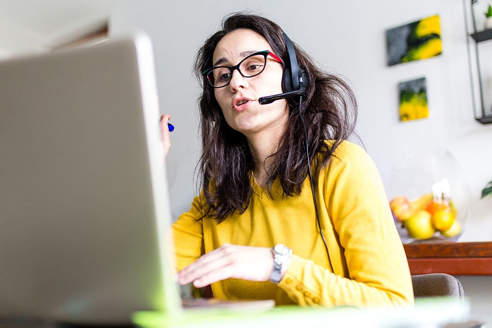 Woman with glasses working on computer and talking on headset.